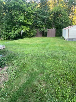 A grassy backyard with a shed and a garage.
