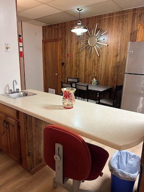A kitchen with a long countertop, a sink, a refrigerator, and a dining area with chairs and a table.