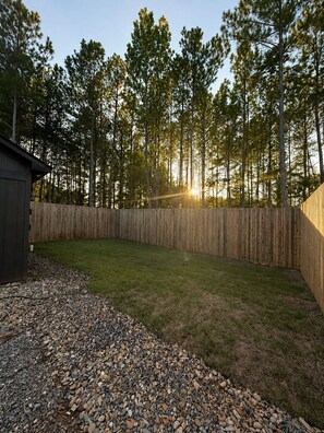 A backyard with a wooden fence, a shed, and a lawn with pebbles.