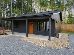 A modern house with a dark exterior, a single orange door, and a covered porch area.
