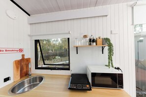 A kitchen with a stainless steel sink, a microwave, a no-smoking sign, and a window with a view of trees.