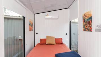 A bedroom with a bed, a window, an air conditioning unit, and a door.