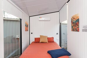 A bedroom with a bed, a window, an air conditioning unit, and a door.