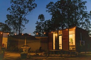 A wooden cabin with a dining area, a barbecue grill, and a large window.