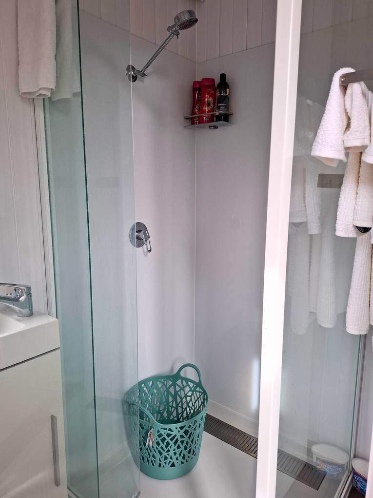 A glass-enclosed shower area with a showerhead, a green basket, and a shelf with toiletries.