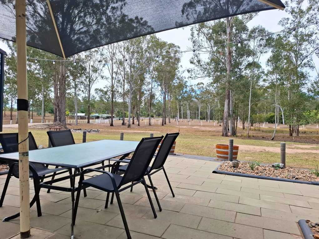 Une terrasse extérieure avec une table et des chaises, entourée d’arbres et d’une pelouse.