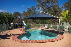 A swimming pool with a slide and inflatable rings, surrounded by a brick deck and metal fencing.