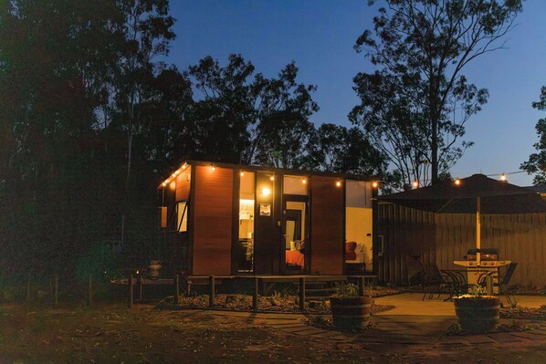 A small wooden cabin with a porch, a grill, and string lights.