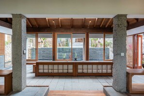 A room with a wooden bench, large windows, and a view of a garden. - Private Villa with Pool and Garden Views (Nusa Lembongan)