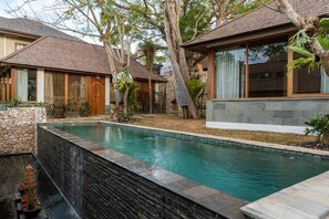 A pool area with a stone wall and a wooden deck. - Private Villa with Pool and Garden Views (Nusa Lembongan)
