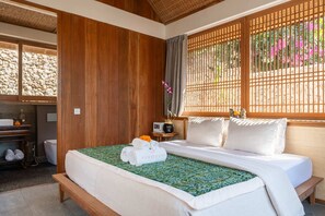 Une chambre d’hôtel avec un lit, un mur recouvert de panneaux en bois, une fenêtre donnant sur des fleurs, une petite table avec une radio et un banc.