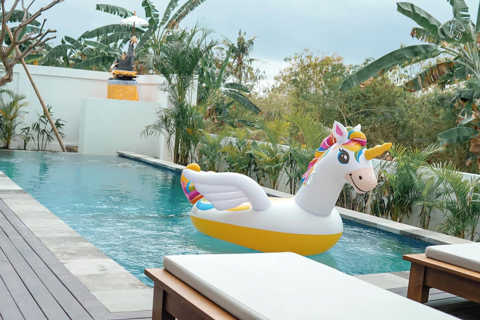 A pool with a unicorn float and lounge chairs.