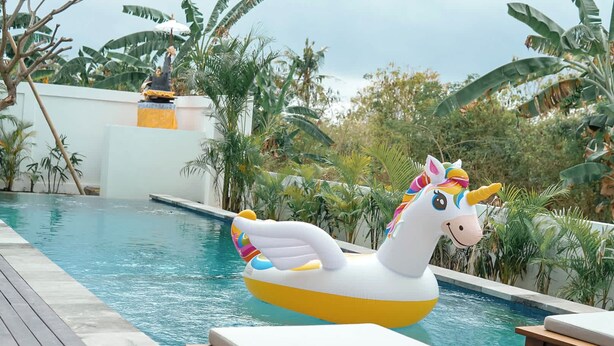 Una piscina con un flotador de unicornio y sillas de descanso.