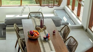 Un comedor con una larga mesa de madera, sillas de mimbre y vistas a la vegetación exterior.