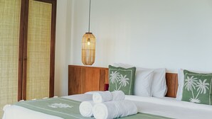 Una cama bien tendida con sábanas blancas y almohadas verdes, una lámpara colgante y un cabecero de madera.