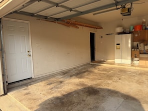 Eine Garage mit weißer Tür, Betonboden und einem Kühlschrank.