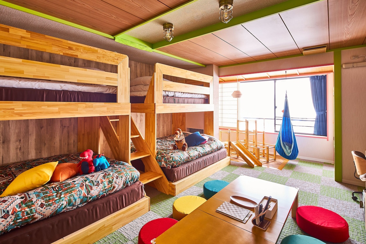 A room with bunk beds, a sofa, a table, and a hanging chair.