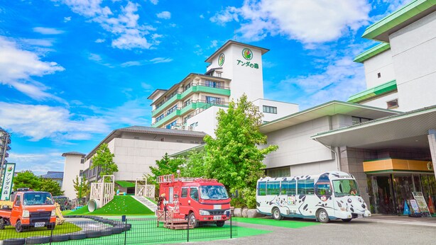 Ein Gebäude mit Grün-Weiß-Farbgebung, ein roter LKW und ein weißer Bus vor dem Haus.