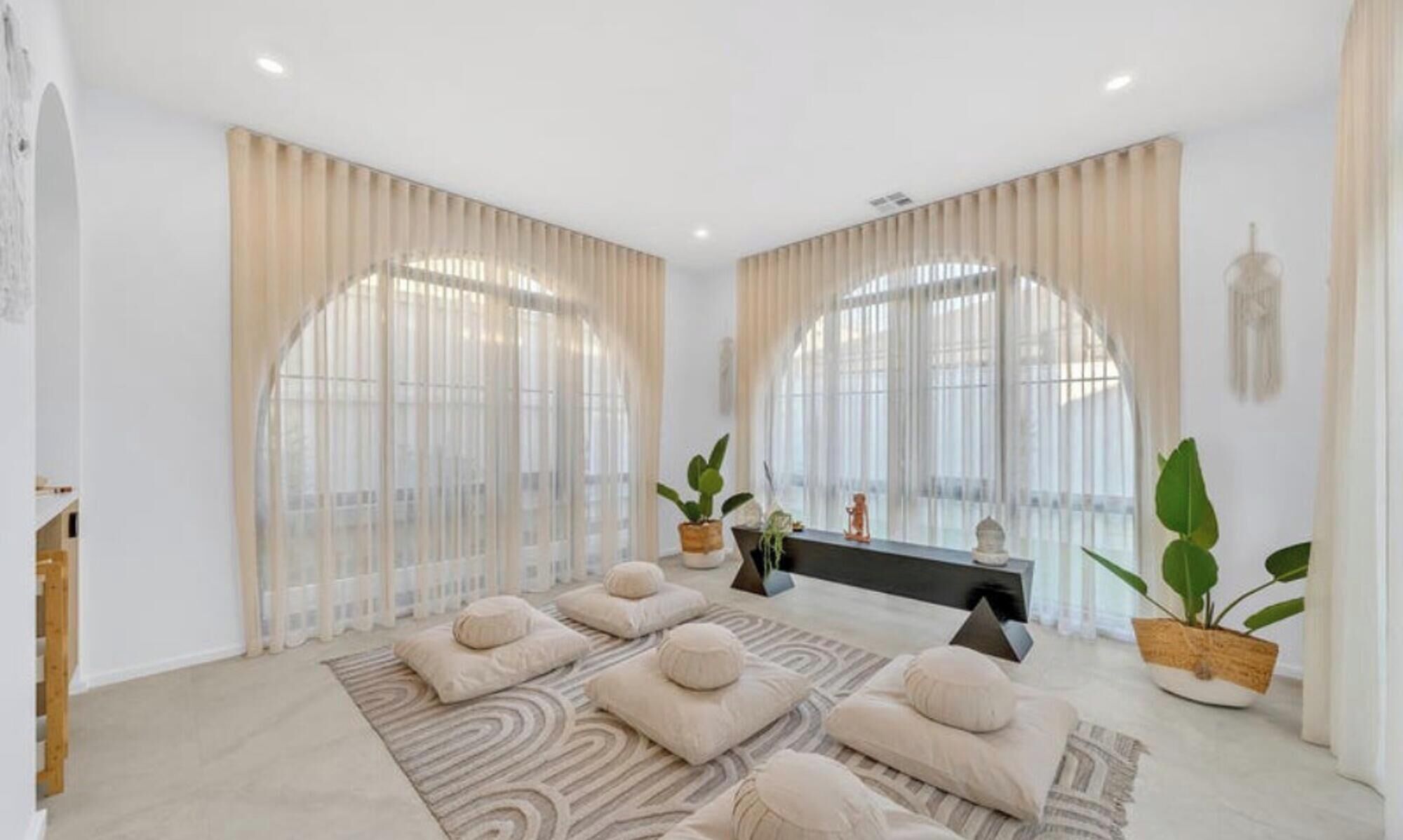 A spacious room with large arched windows, a black console table, and multiple cushions on a patterned rug.