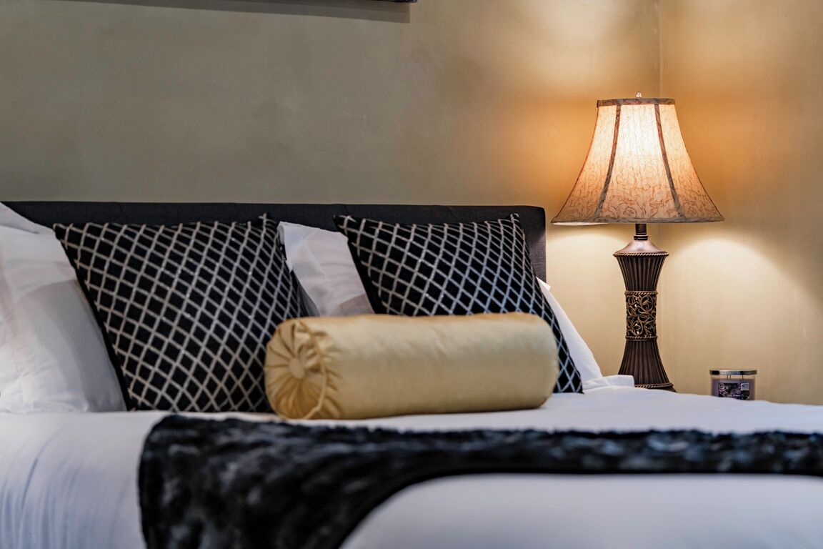 A neatly made bed with a patterned headboard, a bedside lamp, and a small container on the nightstand.