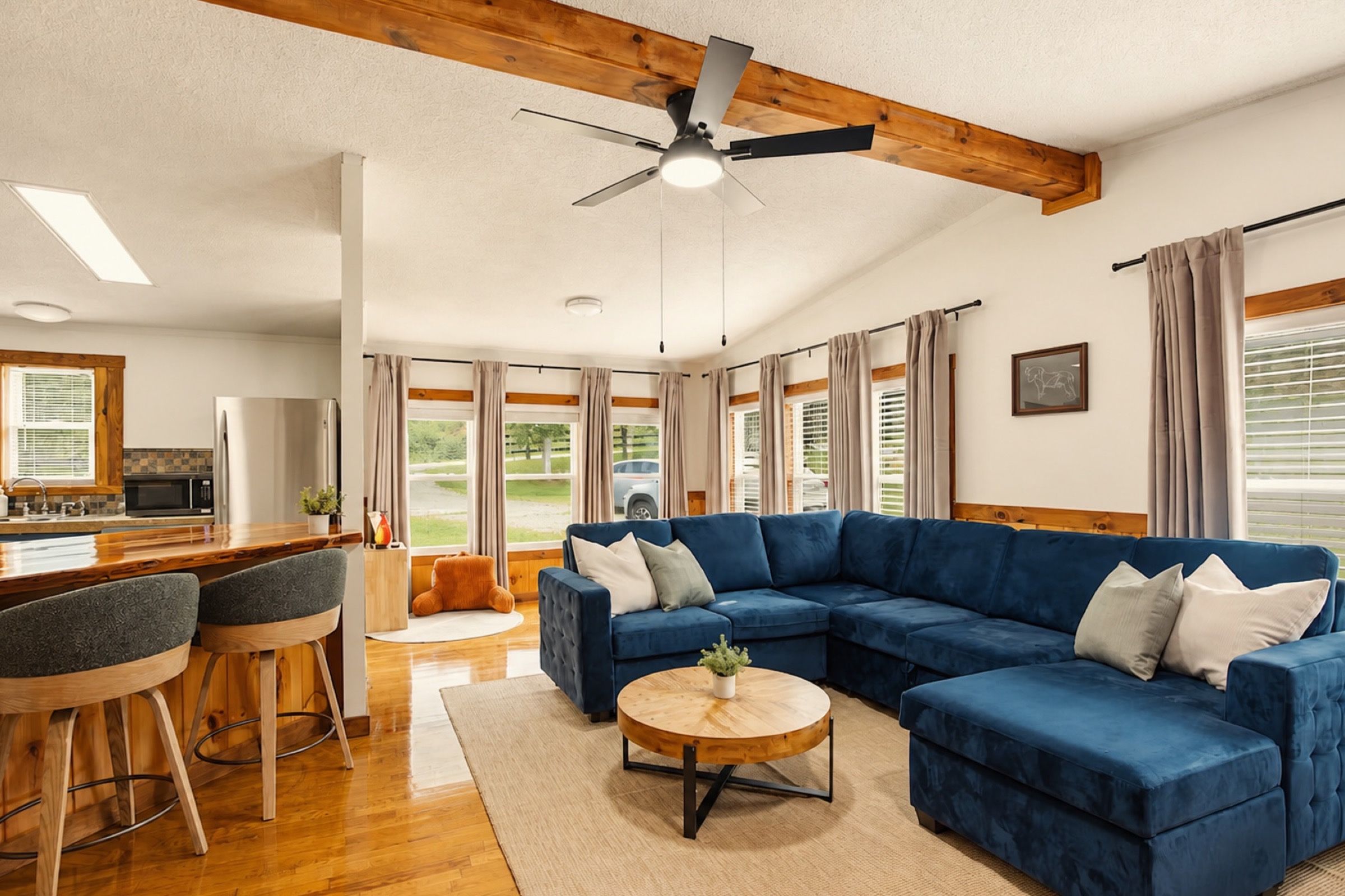 A spacious living area with a blue sectional sofa, a round coffee table, and a dining area with a kitchen in the background.
