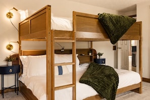 A bunk bed with a wooden frame, white bedding, and a green throw blanket. There are bedside tables with lamps and a small plant on one side. - NEW! Hot Tub + Sauna, Game Room, Near Red River Gorge (Stanton)