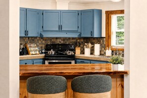 A kitchen with blue cabinets, a black stove, and a wooden bar with two cushioned stools.