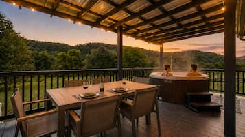 A wooden deck with a table and chairs, a hot tub, and a view of a forested hillside.