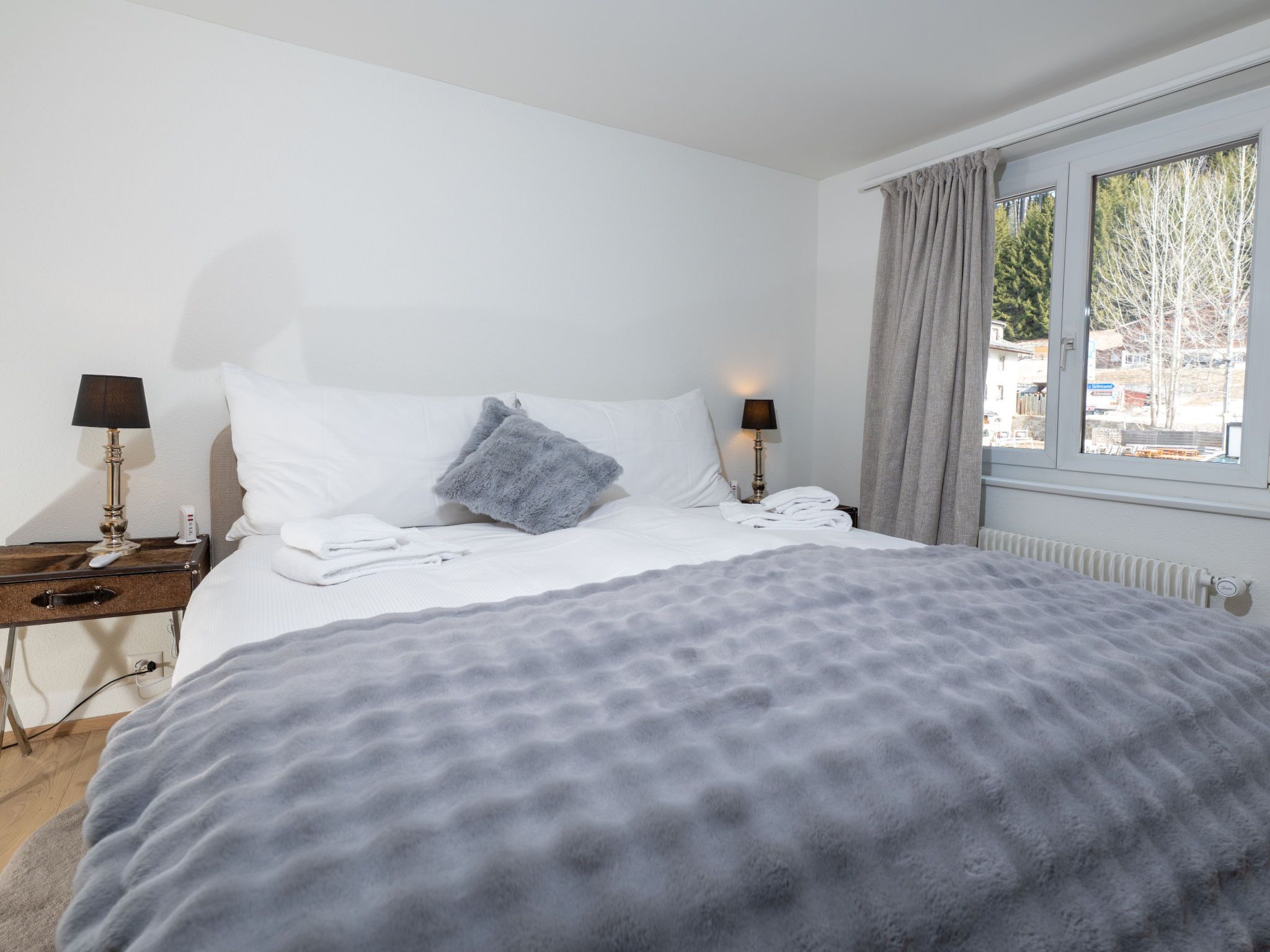 Habitación de hotel con cama, dos lámparas de noche, ventana con cortinas y vista al exterior.