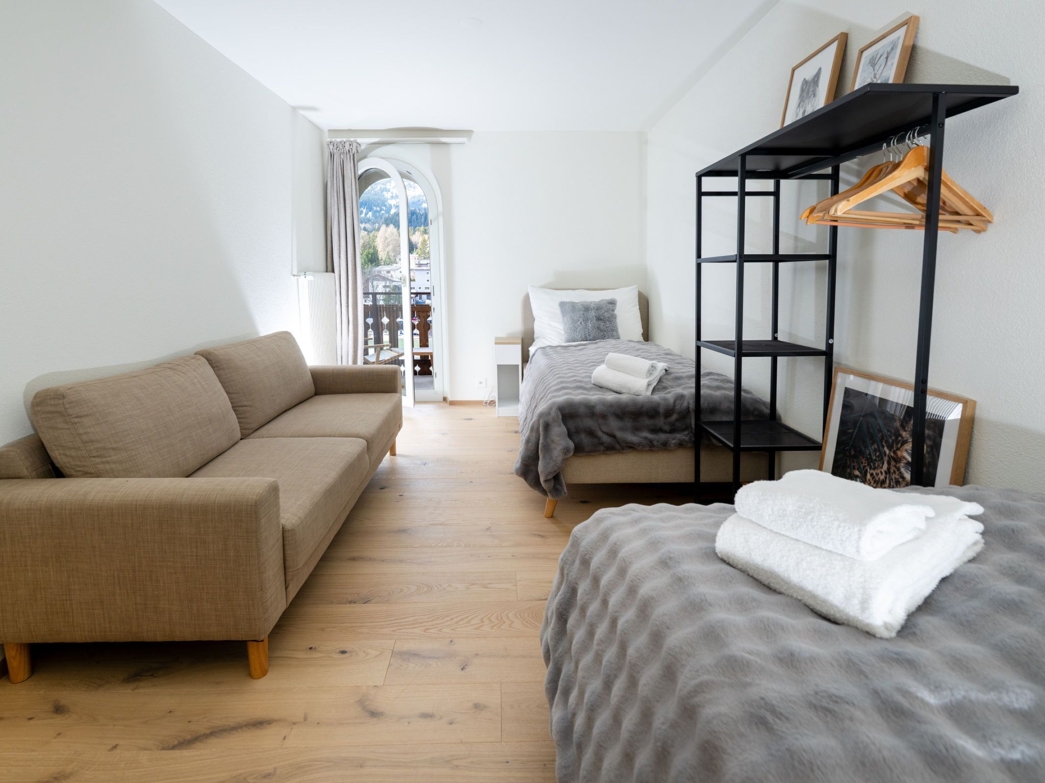 A modern bedroom with a sofa, a bed, a hanging clothes rack, and a view through a window.