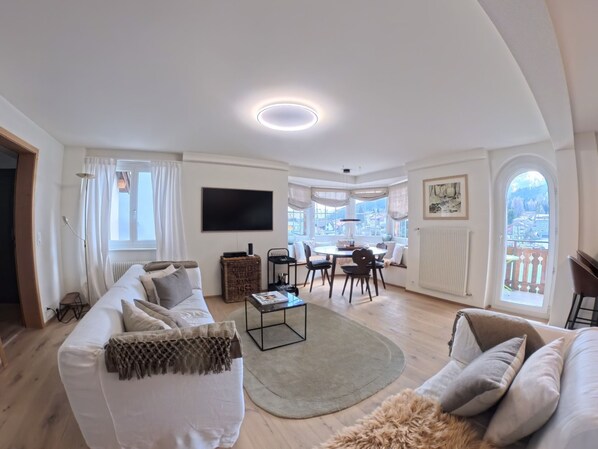A modern living room with a sofa, coffee table, and dining area. - 1624 Aurora 5.5 by Interhome (Vaz)