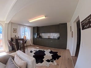 A modern living space with a kitchen, dining area, and a large window. - 1624 Aurora 5.5 by Interhome (Vaz)