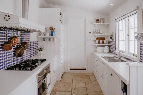 A kitchen with white cabinets, a stove, and a sink. There are decorative tiles on the wall and a window with a view.