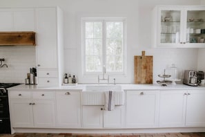 Una cucina con mobili bianchi, una finestra, un tagliere di legno e una macchina per il caffè.