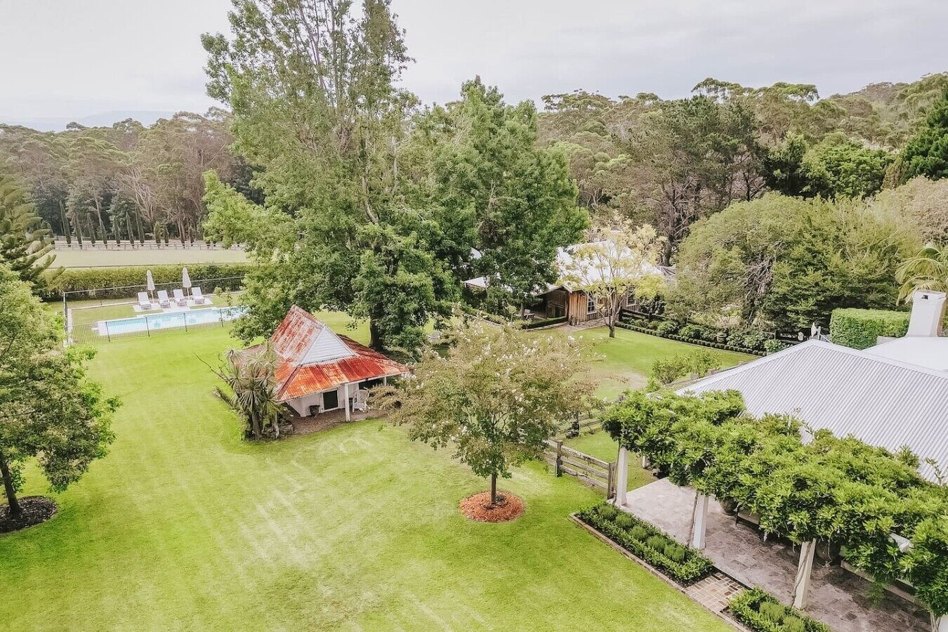 A residential property with a swimming pool, a red-roofed building, and a well-maintained lawn.
