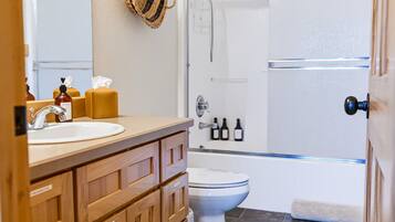 Un baño con tocador de madera, inodoro blanco, cabina de ducha y un espejo grande.
