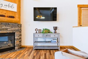 A living room with a stone fireplace, a mounted television, and a wooden coffee table.