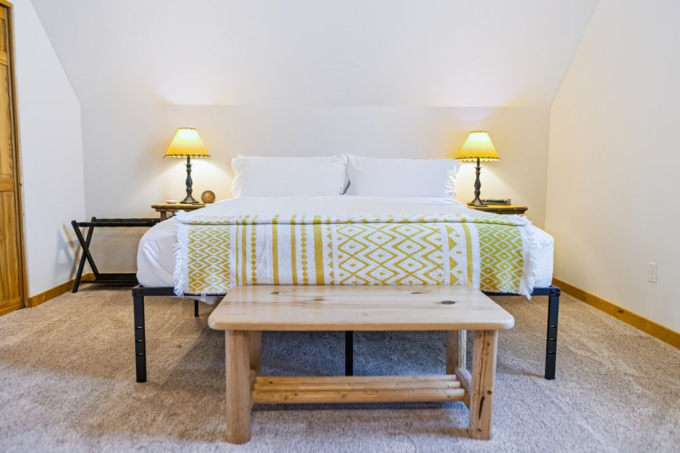 Ein Schlafzimmer mit einem Bett, zwei Nachttischlampen, einer Holzbank und einem kleinen Tisch.