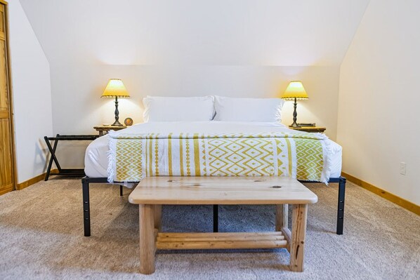 A bedroom with a bed, two bedside lamps, a wooden bench, and a small table.