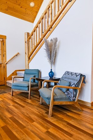 A wooden staircase with a wooden railing, two blue upholstered chairs, a small table with a vase, and a patterned throw on one of the chairs.