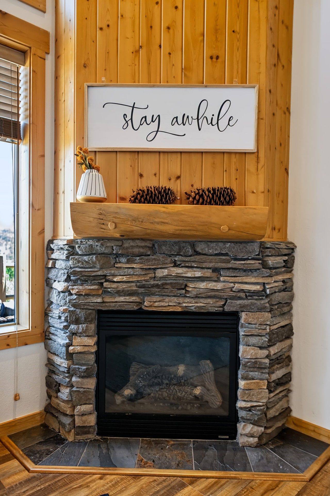 A stone fireplace with a wooden mantel, a framed sign above it, and a window to the left.