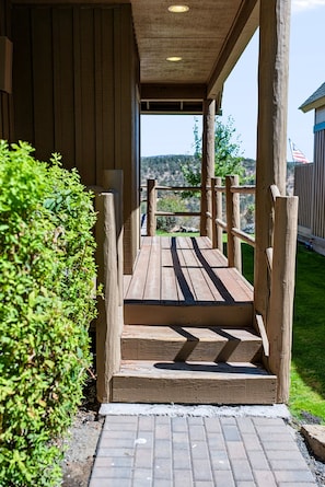 Una terrazza in legno con gradini che conducono a una zona coperta, immersa nel verde e con una vista aperta sul paesaggio.