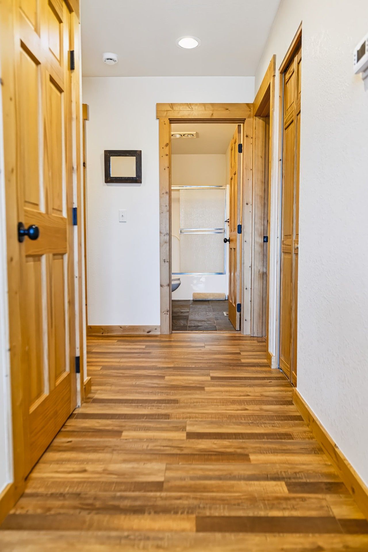 Un couloir doté d’un plancher en bois et de portes menant à une salle de bain.