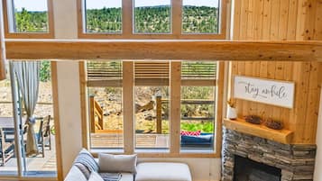 A spacious living area with a large sectional sofa, a stone fireplace, and a view of a natural landscape through large windows.
