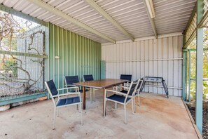 Zona exterior coberta amb taula i caires, una barbacoa i una tanca amb plantes.