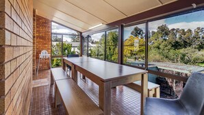 A covered outdoor seating area with a table and benches, large windows offering a view of trees and a garden. - The Shire Retreat, Dubbo (Dubbo)