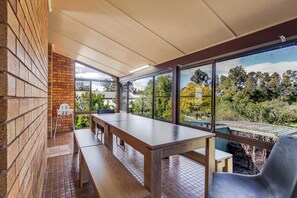 A covered outdoor seating area with a table and benches, large windows offering a view of trees and a garden. - The Shire Retreat, Dubbo (Dubbo)