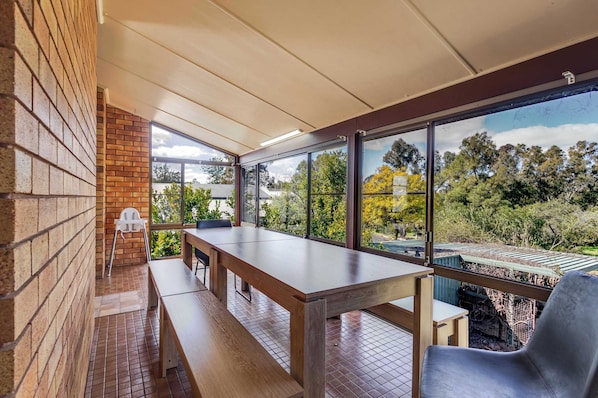 A covered outdoor seating area with a table and benches, large windows offering a view of trees and a garden. - The Shire Retreat, Dubbo (Dubbo)