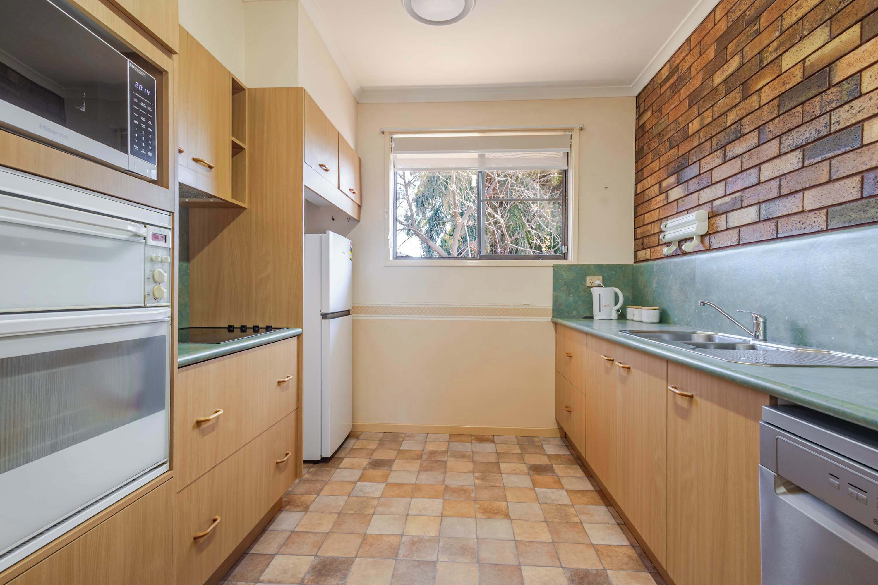 Una cucina compatta con mobili in legno, forno integrato, frigorifero, una finestra e una parete in mattoni.