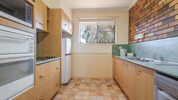 Una cucina compatta con mobili in legno, forno integrato, frigorifero, una finestra e una parete in mattoni.